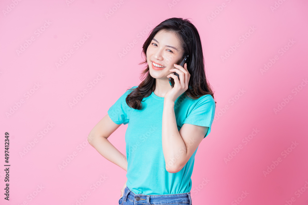 年轻的亚洲女性在粉色背景下使用智能手机