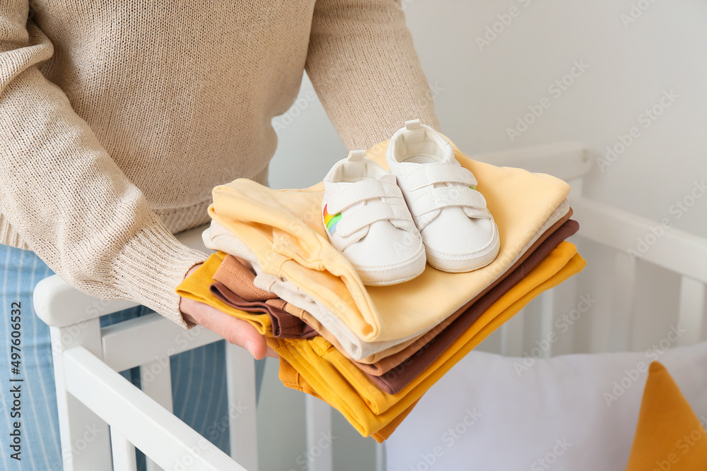 女人在家里的婴儿床上放婴儿衣服和婴儿靴