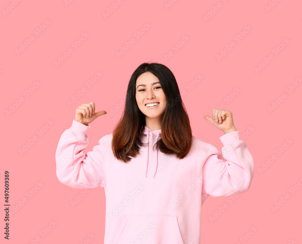 身穿连帽衫的亚洲年轻女子在粉色背景上竖起大拇指