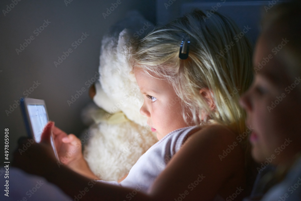 睡前互动性更强。两个小女孩在睡前使用数字平板电脑的照片