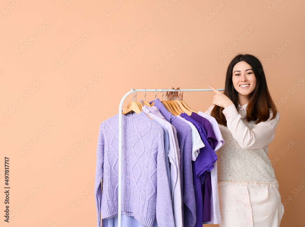 一个年轻的亚洲女人指着什么东西，把米色背景的紫色衣服放在架子上