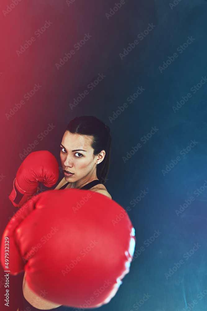 Knock them out. Shot of a young woman wearing boxing gloves against a dark background.