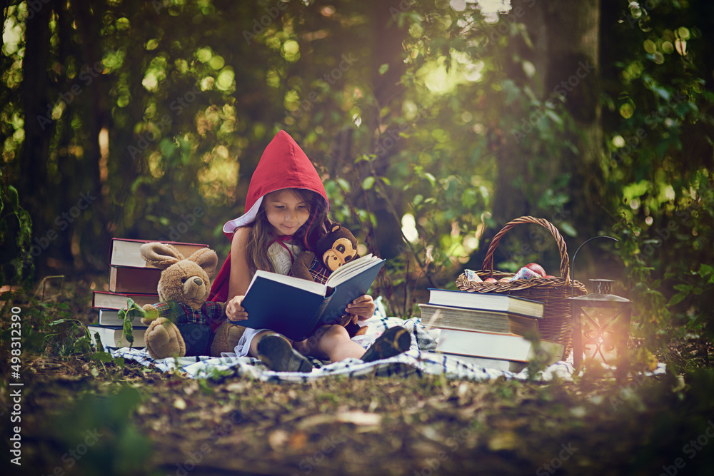 Books can transport us to the most magical places. Shot of a little girl in a red cape reading a boo