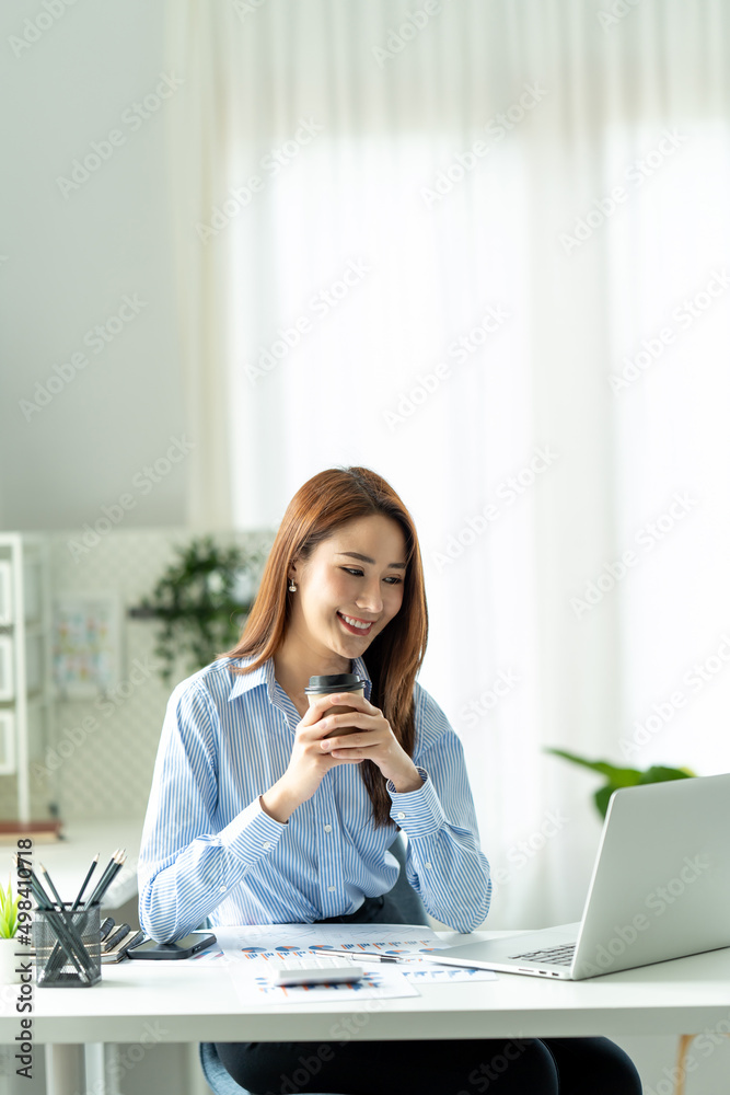年轻漂亮的女人坐在工作场所的椅子上使用笔记本电脑。