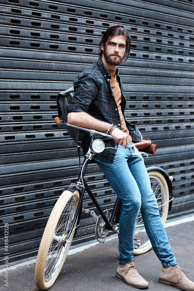 他绝对是一个潮流引领者。一个英俊的年轻人坐在户外自行车上的全景照片