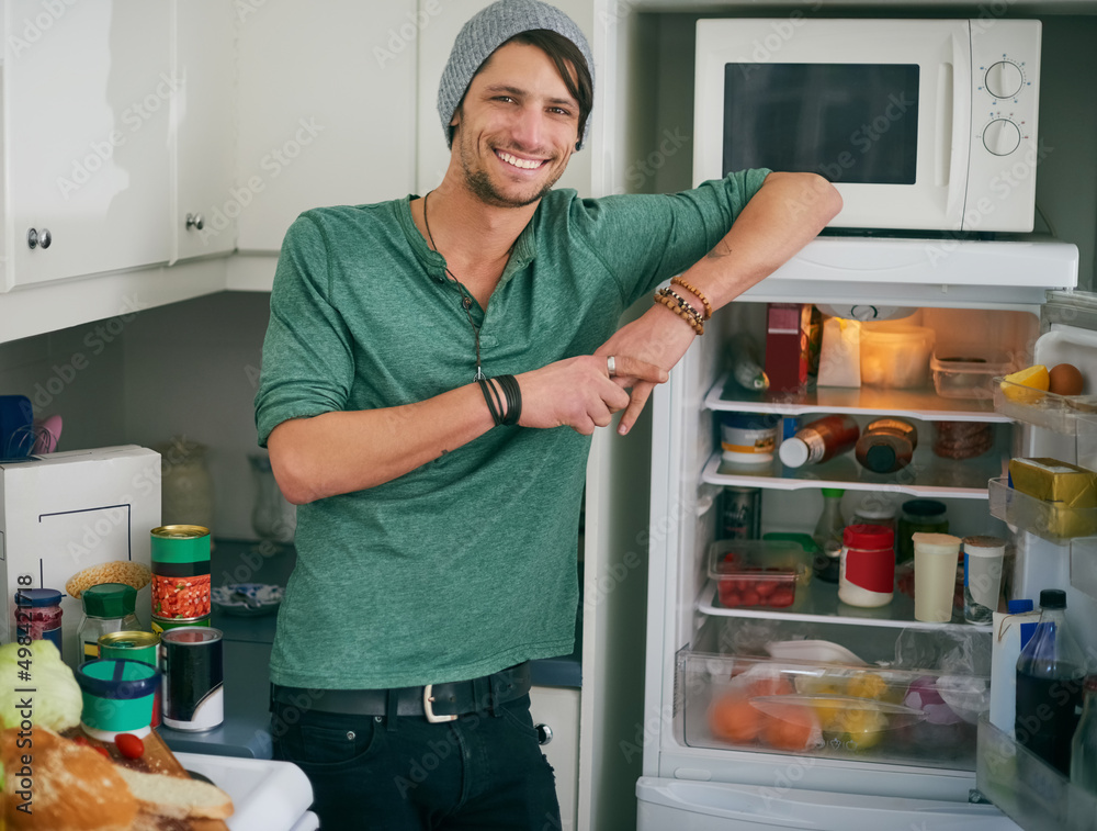 想吃点零食。一个微笑的年轻人站在厨房打开的冰箱旁的画像。