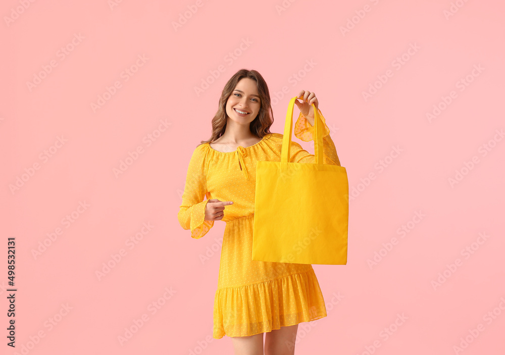 漂亮的年轻女人指着粉色背景的黄色环保袋
