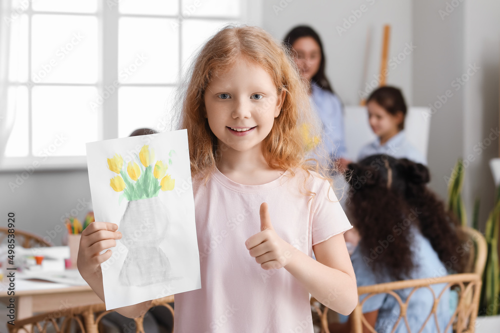 可爱的红发女孩在艺术大师课上竖起大拇指，举着画的画