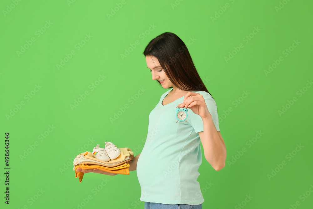 年轻孕妇，绿色背景上有一叠婴儿衣服和闹钟