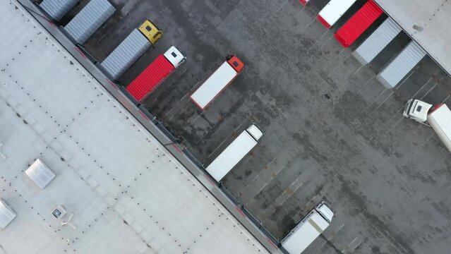 Aerial top down view of semi-trailers trucks stand at warehouse ramps for loading and unloading goods in a logistics park