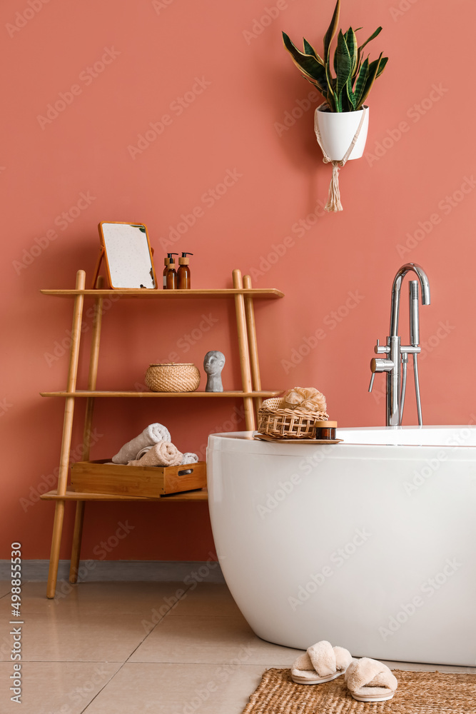 棕色墙壁附近的现代浴缸和带用品的架子