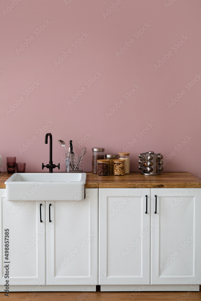 粉色墙壁附近带水槽、厨具和食物的柜台