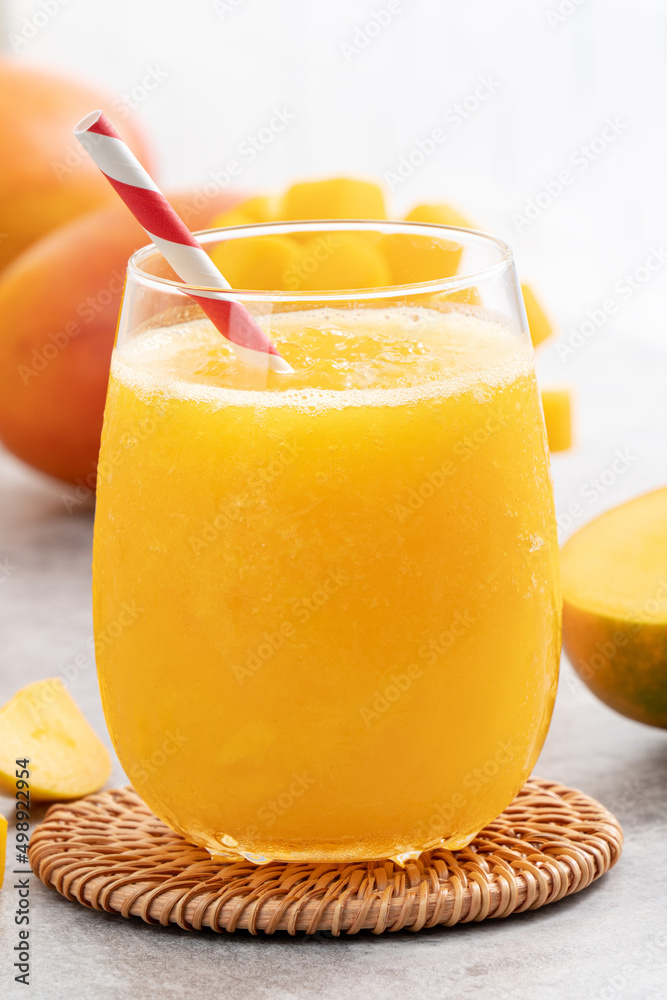 新鲜美味的芒果汁奶昔，装在灰色桌子背景的玻璃杯里。