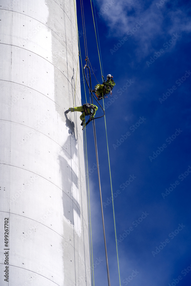 两名工业登山者从烟囱上爬下来，用特殊设备清理涂鸦破坏行为。