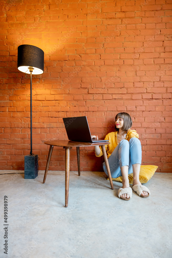 一名年轻女子在笔记本电脑上工作，放松地坐在砖墙后面的咖啡桌旁