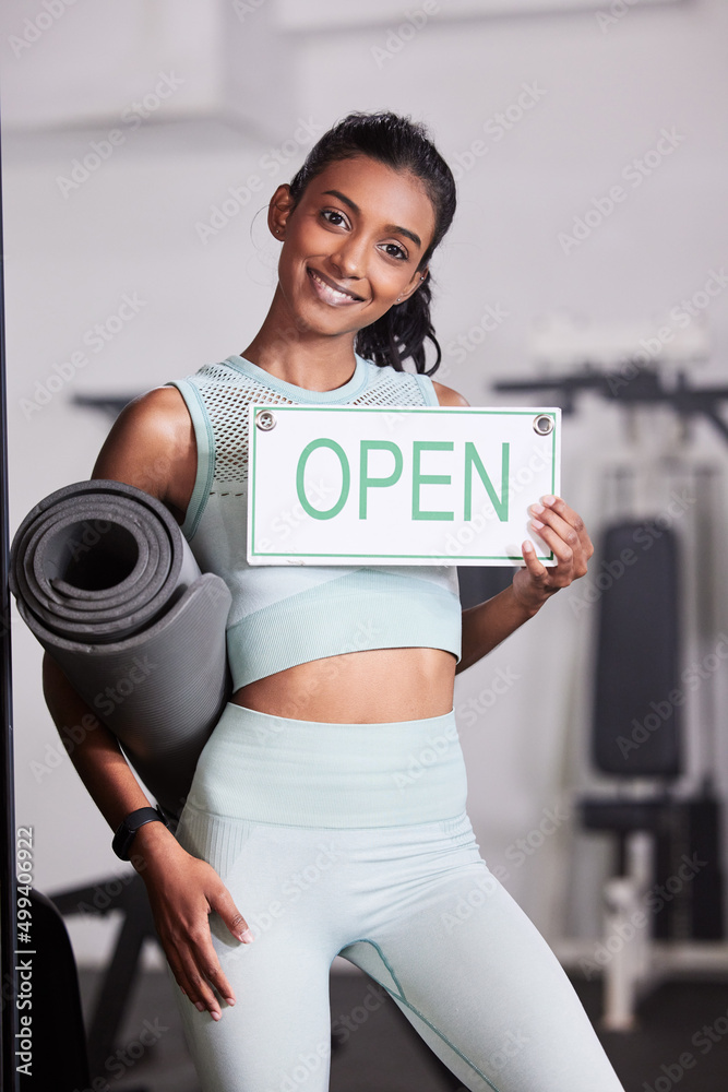 让我们帮你找回光彩。一位年轻女子在健身房举着一块开放的牌子的画像。