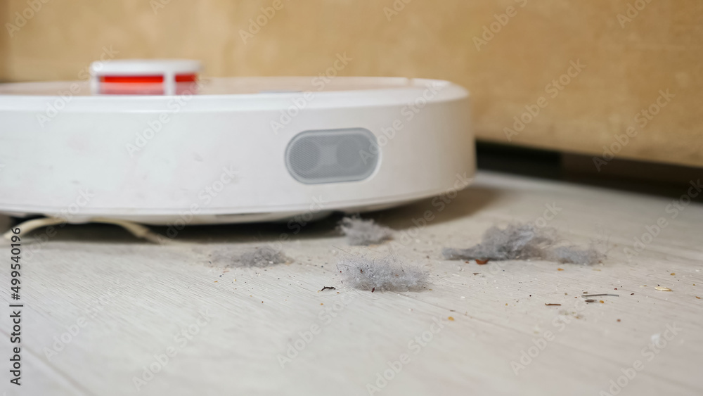 机器人吸尘器骑在地板上，在客厅沙发附近吸尘，特写