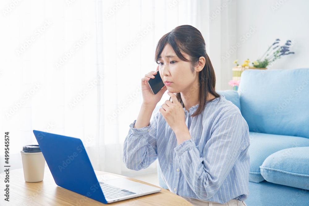 女性　ノートパソコンを見て電話する　リビング