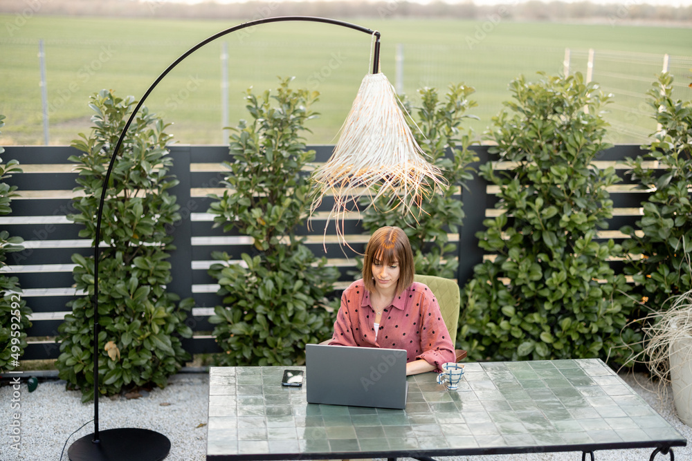 一名年轻女子在花园的户外工作空间用笔记本电脑工作。在被子里远程工作的概念