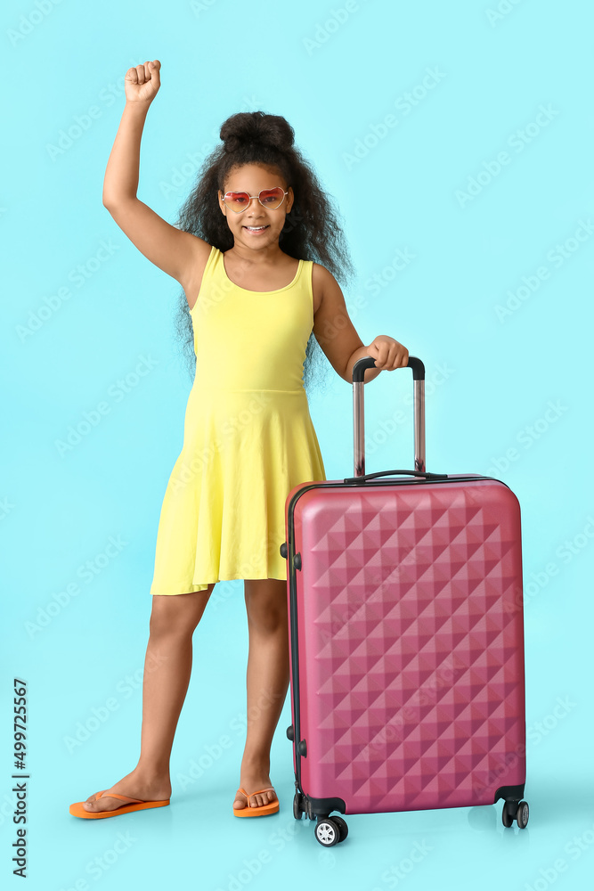 带着蓝色背景行李箱的快乐的非洲裔小女孩