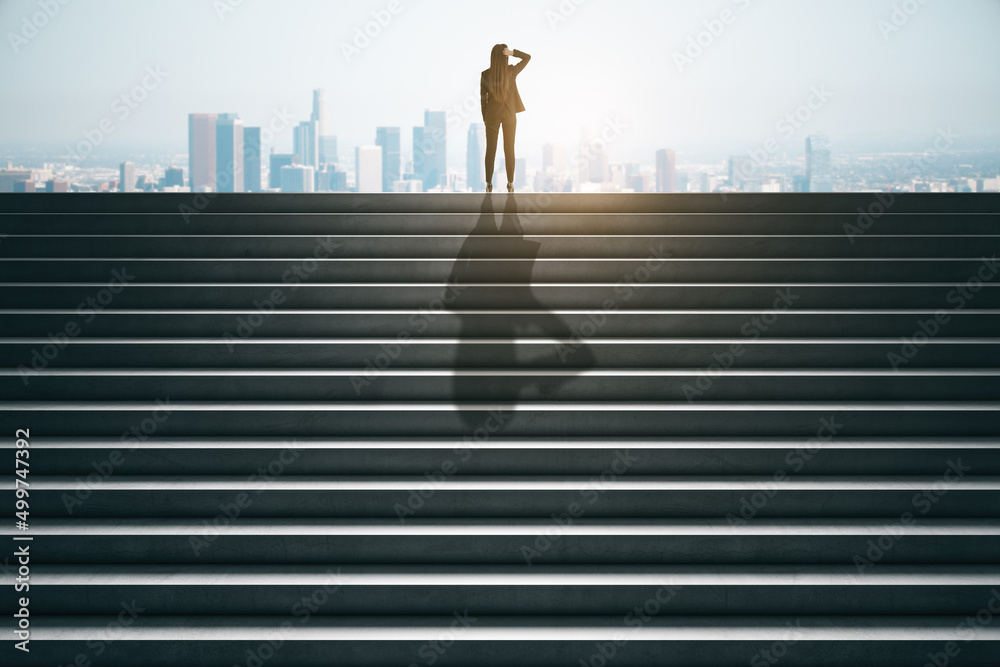 女商人在水泥楼梯顶上的后视图，在城市的阳光下眺望远方