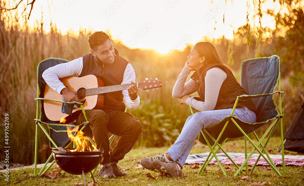 Life is better around the campfire. Shot of a you man playing his guitar to his wife outside while c