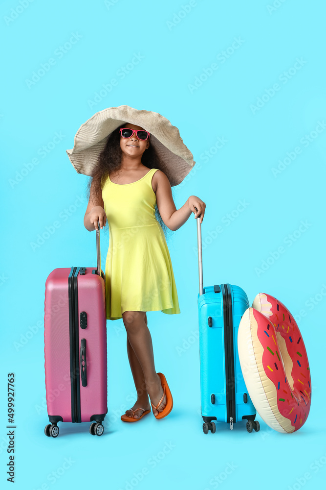 可爱的非裔美国小女孩，蓝色背景，带着行李箱和充气环