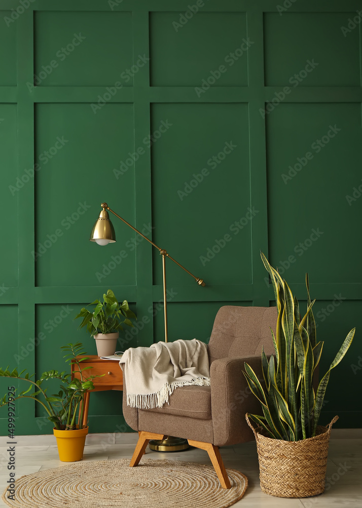 绿色墙壁附近舒适的扶手椅、室内植物和现代灯具