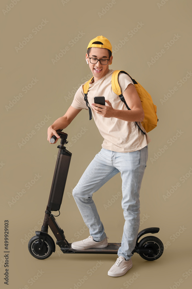 亚洲男学生骑着电动自行车在彩色背景下使用手机