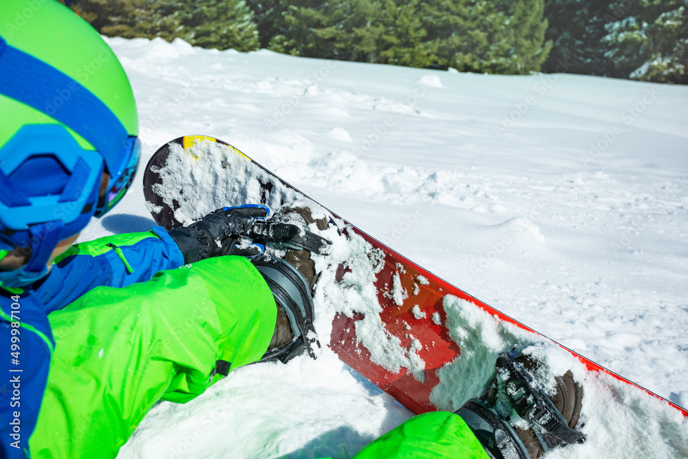 男孩坐在雪地里连接滑雪板的特写