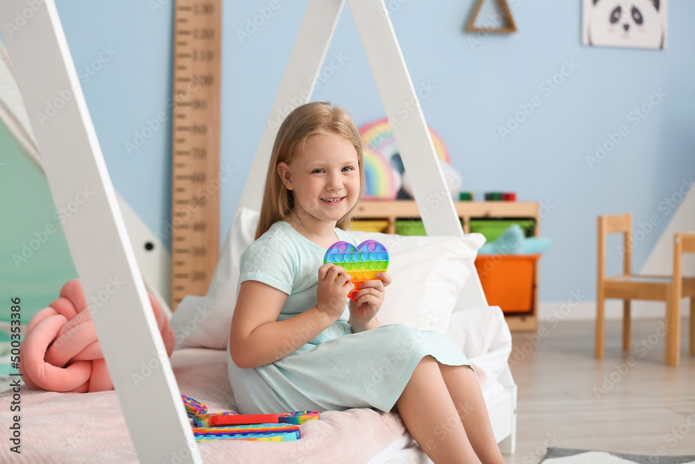 快乐的小女孩坐在床上，手里拿着心形玩具，在儿童房里坐立不安