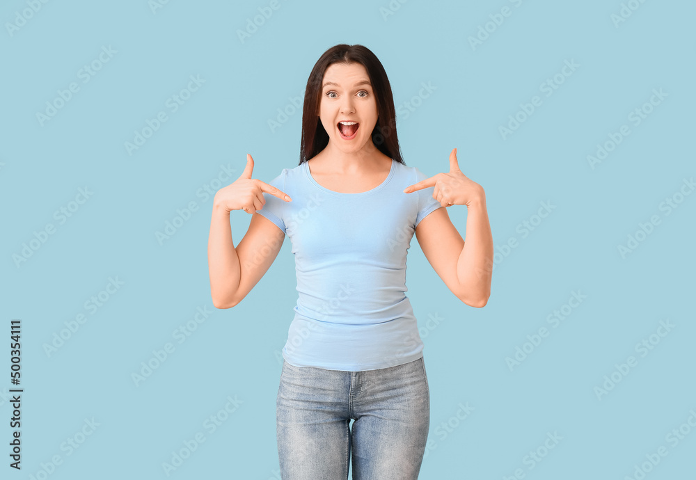 快乐的年轻女人指着蓝色背景的t恤