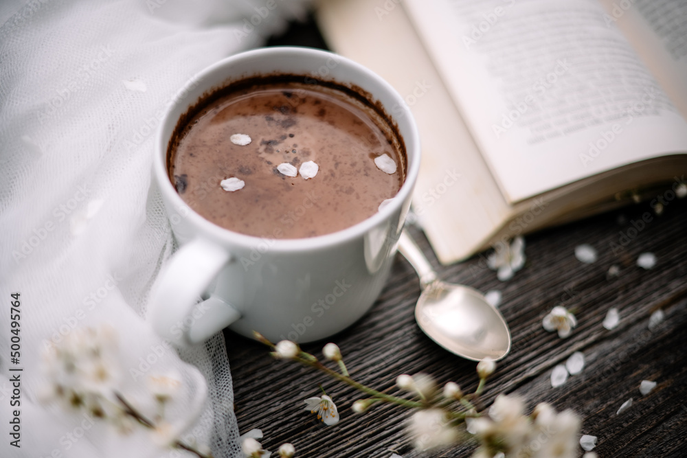一杯热巧克力可可、旧书和木制背景的春天樱花。阅读概念