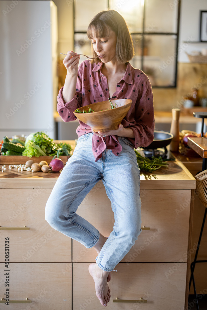 一个穿着休闲的年轻快乐女人坐在桌子上吃健康沙拉的画像