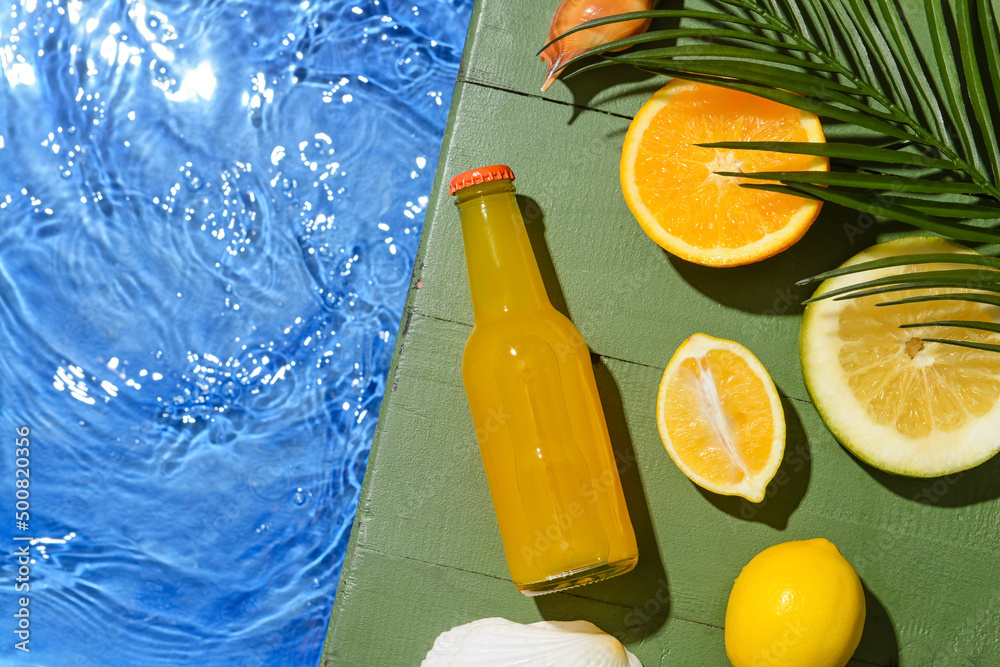 一瓶美味的苏打水，配水果和热带树叶，靠近游泳池