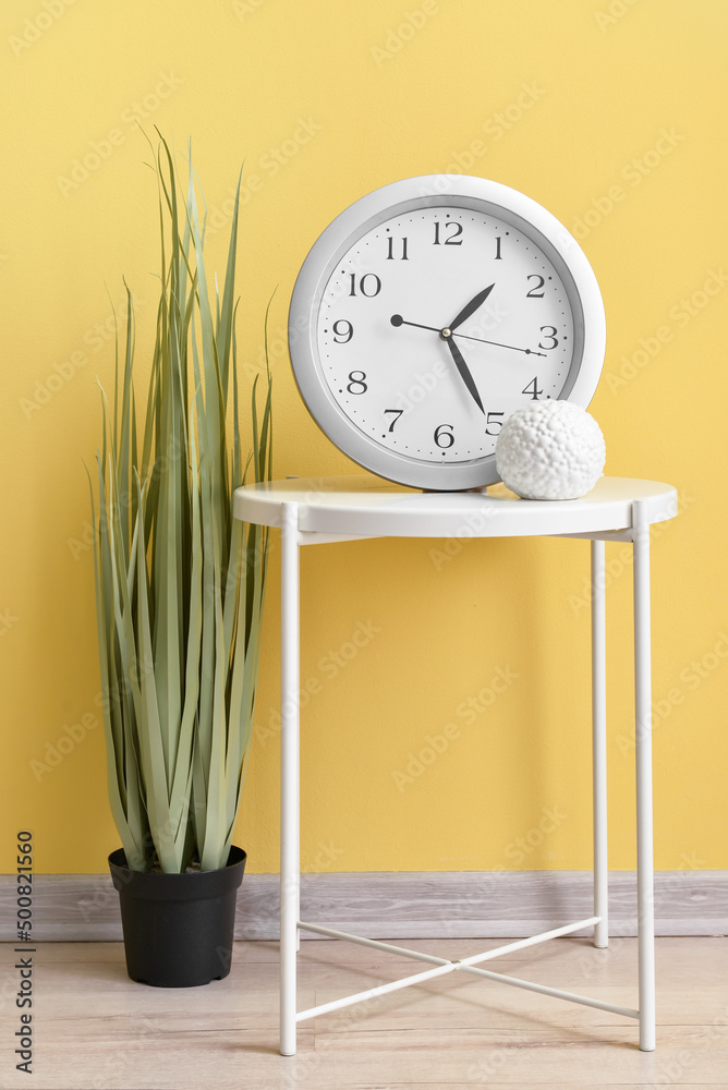 房间彩色墙上有新的现代时钟和室内植物的桌子
