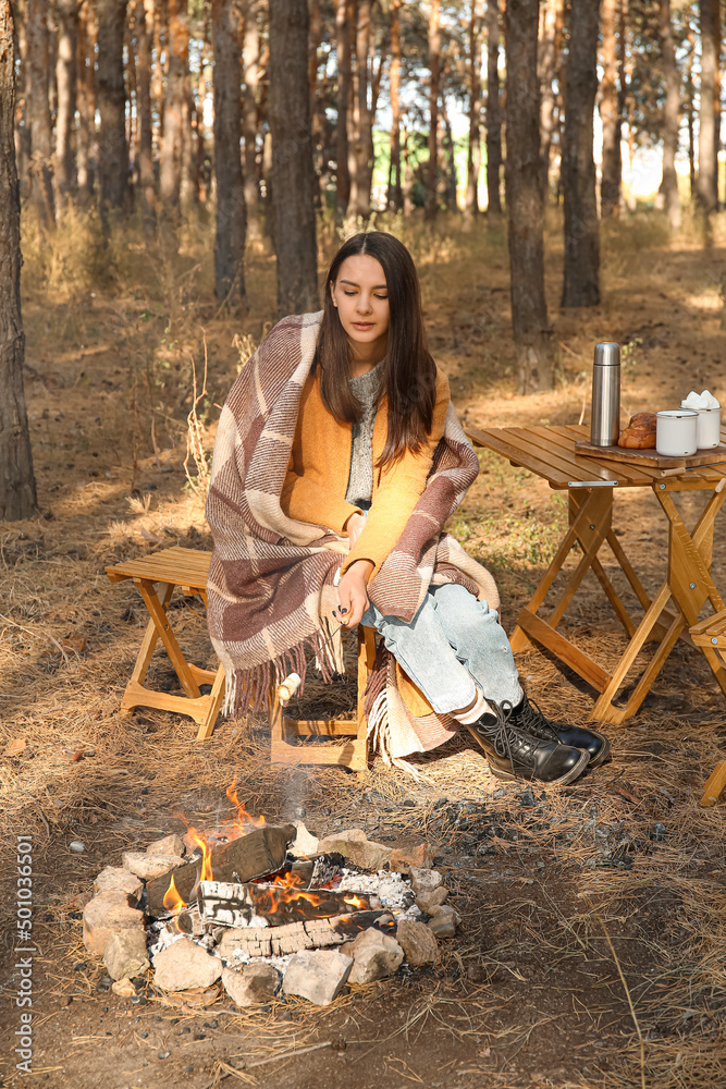 Woman roasting marshmallows on fire in autumn forest