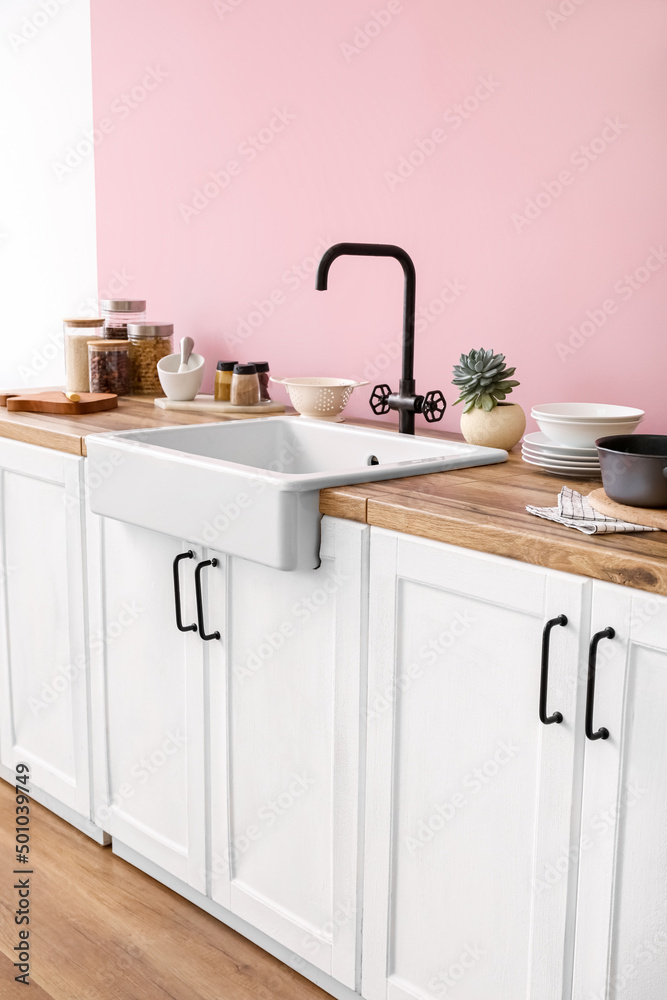 粉色墙壁附近的带陶瓷水槽和厨房用具的柜台