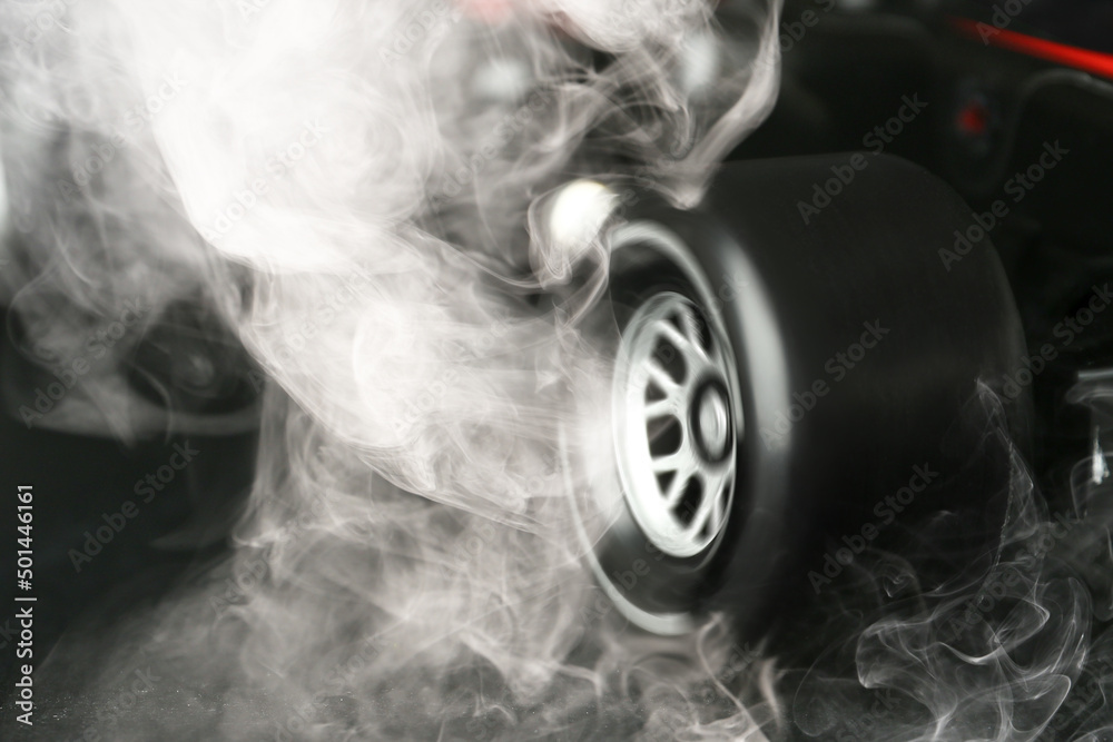 黑色背景下车轮下冒出烟雾的现代赛车，特写