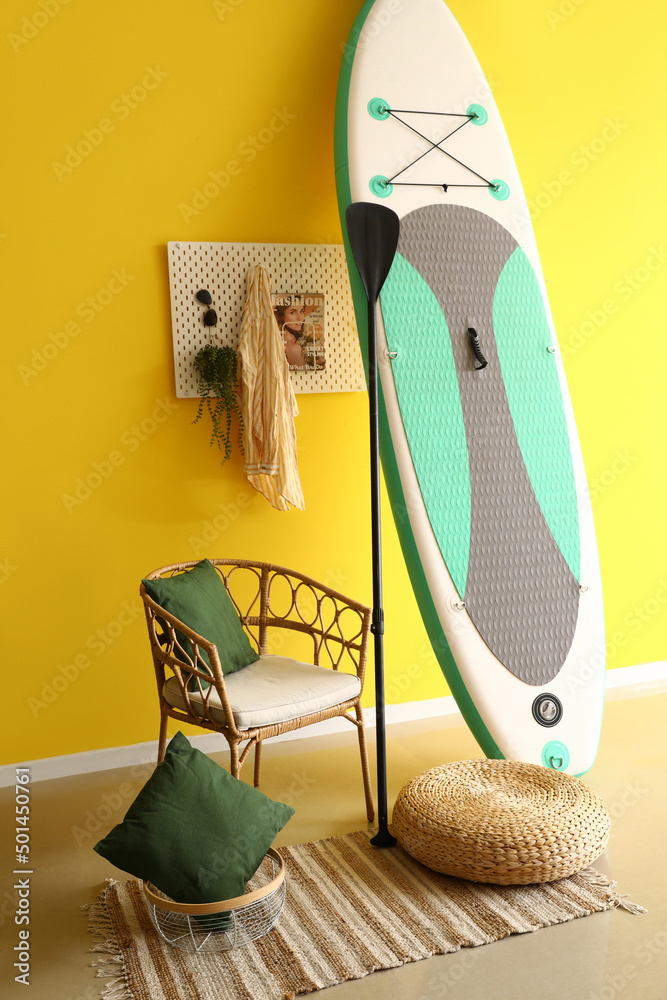 舒适的椅子、桨板和冲浪板，可在室内黄色墙壁附近冲浪