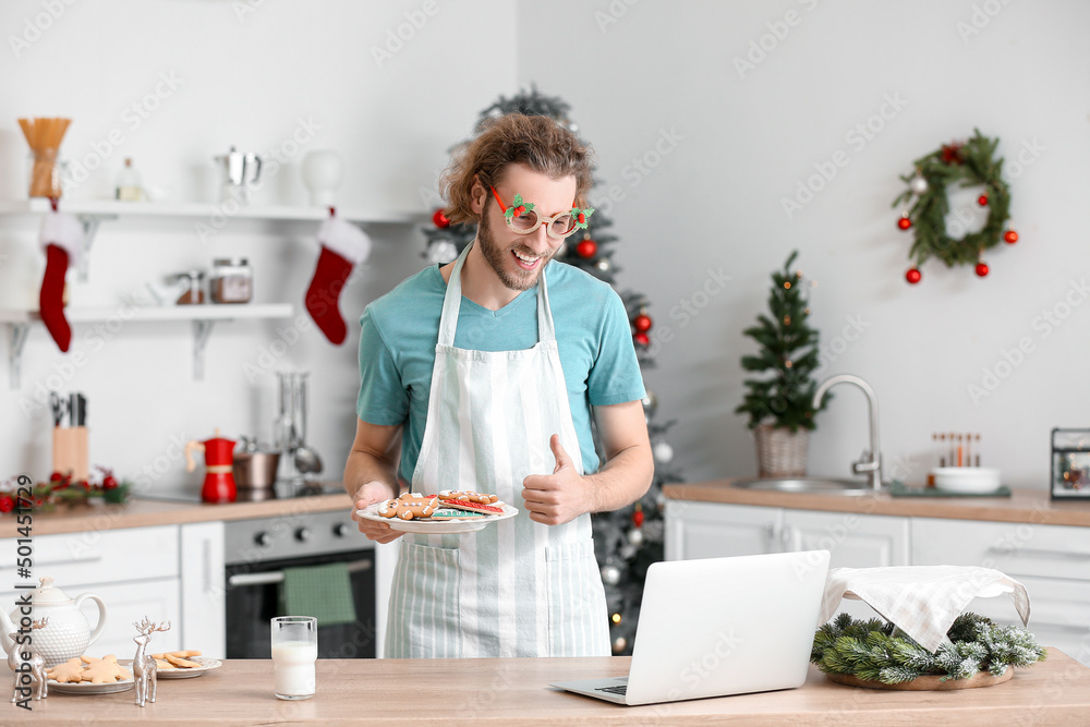 圣诞节前夕，一个拿着姜饼饼干的年轻人在厨房里竖起大拇指