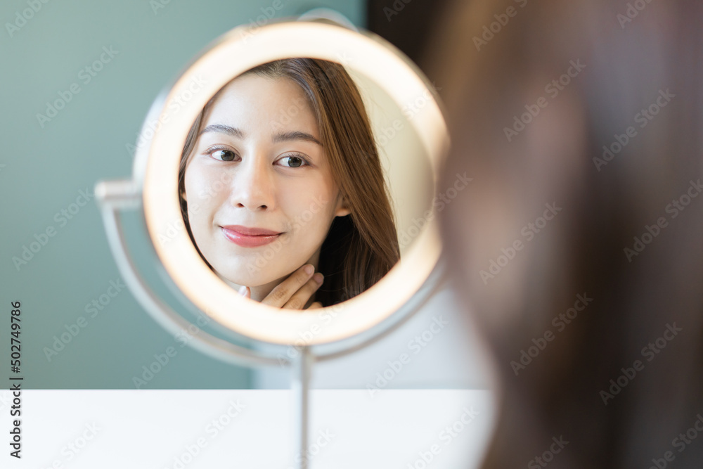 清新、健康的皮肤，美丽的亚洲年轻女性，女孩看着镜子，抚摸她的脸