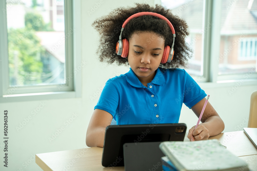 戴着耳机的非洲裔美国女孩在家里用电脑看视频课，戴着耳机快乐的孩子
