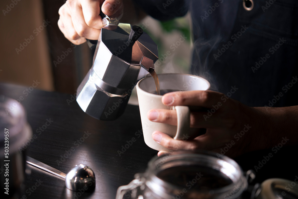 咖啡师将摩卡壶咖啡机中的咖啡倒入咖啡杯。手持意大利经典摩卡