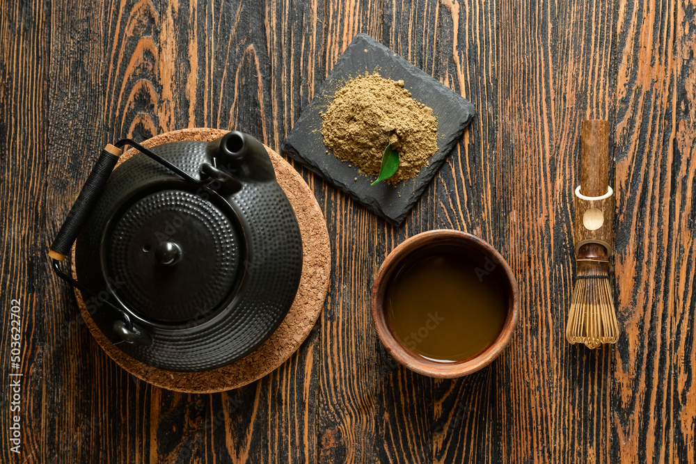 Teapot, chasen, powdered matcha tea and cup of beverage on wooden background