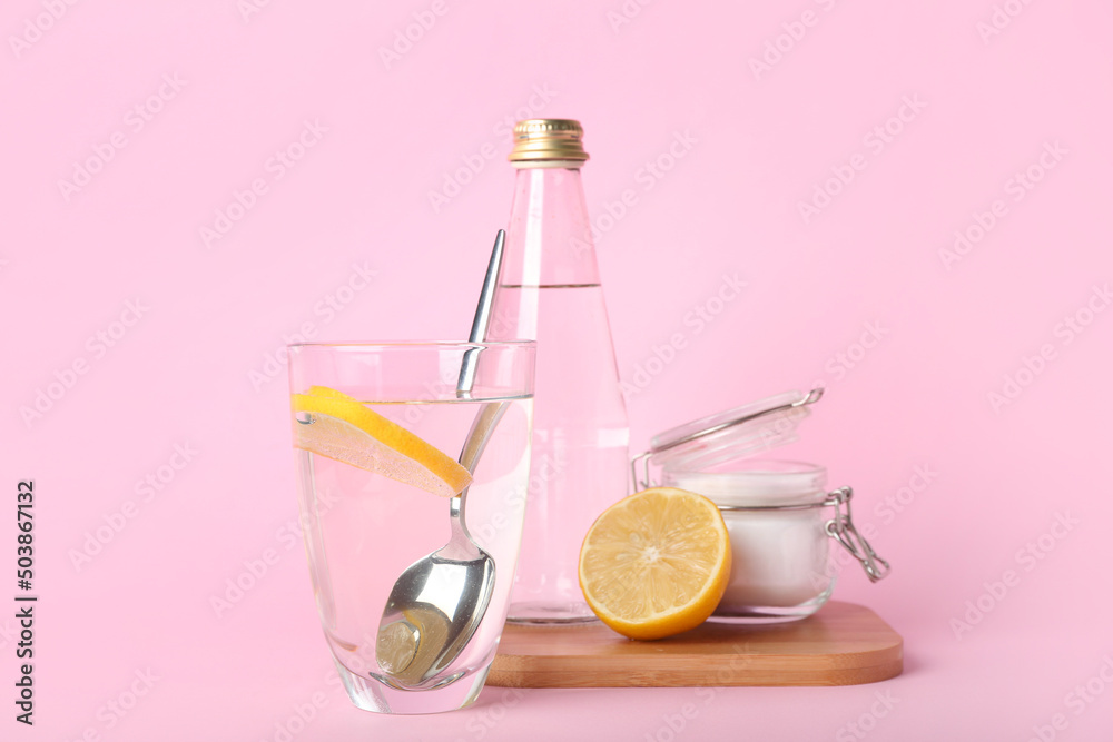 一杯粉红色背景的水、小苏打和柠檬