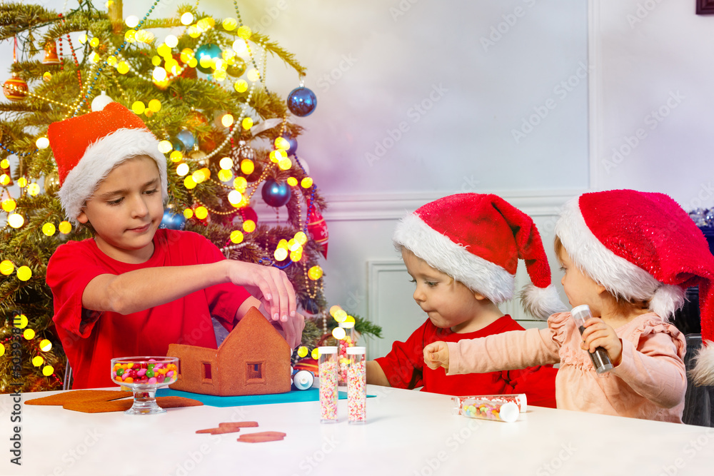孩子们戴着圣诞老人帽一起装饰姜饼屋