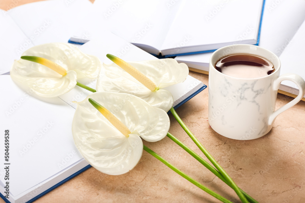 Beautiful anthurium flowers with books and cup of coffee on color background, closeup
