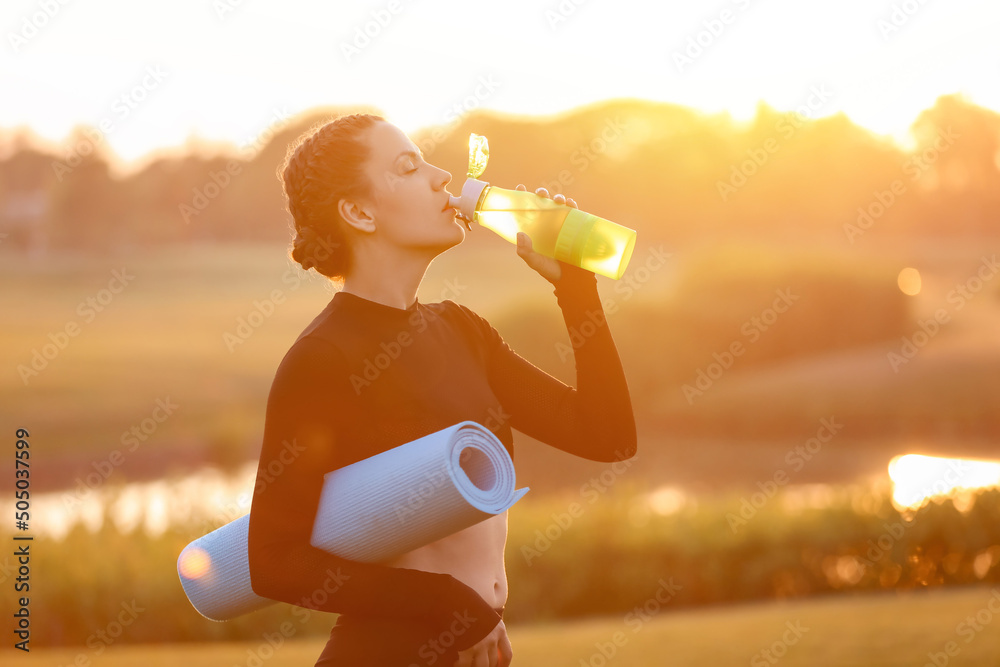 美丽的年轻女子在户外练习瑜伽后喝水