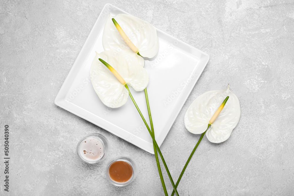 Plate with beautiful anthurium flowers and glasses of coffee on light background